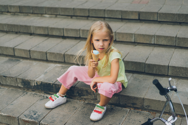 cute child with ice cream sitting on city steps alone - Foto, afbeelding