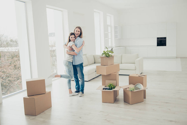 We did it! Rent property happiness furniture concept. Joyful lovely rejoicing beautiful handsome cheerful people in casual denim clothes standing in white spacious room around open boxes with things - Photo, image