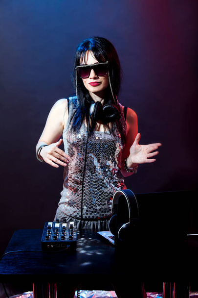 Retrato de DJ jovem sobre fundo vermelho e azul. Mulher DJ com headphne e óculos pretos toca disko música. Festa de glamour no equipamento no clube de verão
. - Foto, Imagem
