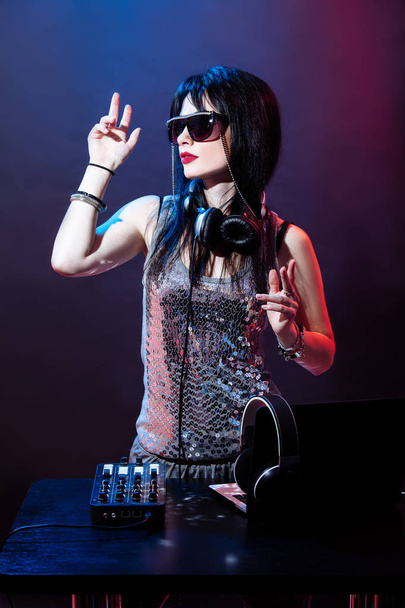 Retrato de DJ jovem sobre fundo vermelho e azul. Mulher DJ com headphne e óculos pretos toca disko música. Festa de glamour no equipamento no clube de verão
. - Foto, Imagem