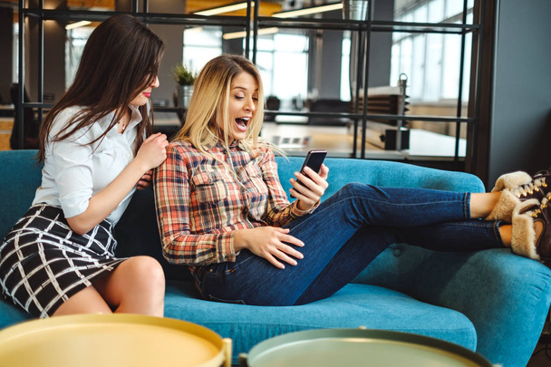 Belos colegas do sexo feminino em pausa surpreendido ao olhar para o telefone móvel
 - Foto, Imagem