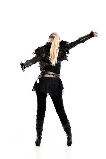 full length portrait of blonde girl wearing torn black feather costume. standing pose with back to the camera, isolated on white background. - 写真・画像