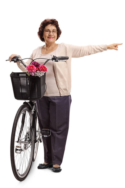 Full length portrait of an elderly woman with a bicycle pointing isolated on white background - 写真・画像