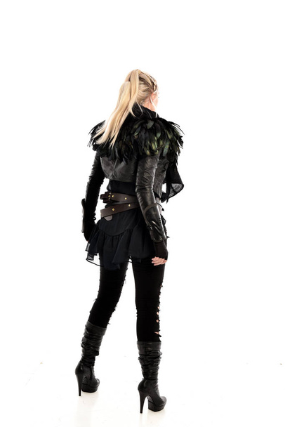 full length portrait of blonde girl wearing torn black feather costume. standing pose with back to the camera, isolated on white background. - Photo, Image