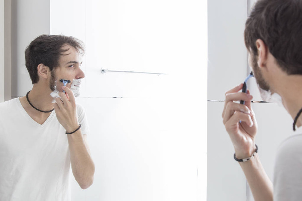 νεαρός άνδρας ο ίδιος κοιτάζοντας καθρέφτη, πρωί ρουτίνα ξυρίσματος  - Φωτογραφία, εικόνα