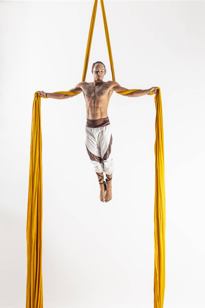 привабливий м'язистий чоловік робить акробатичне виконання з жовтими тканинами на білому тлі
 - Фото, зображення