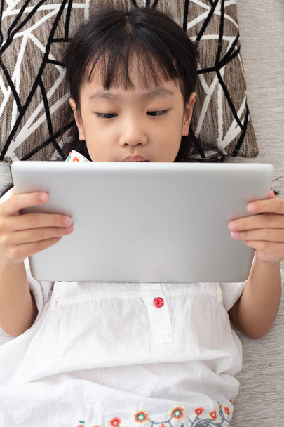 Asian Chinese little girl lying on the sofa and playing tablet in the living room - Foto, immagini