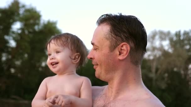Small wet bathing child claps his hands and laughs sitting in embrace of dad - Footage, Video