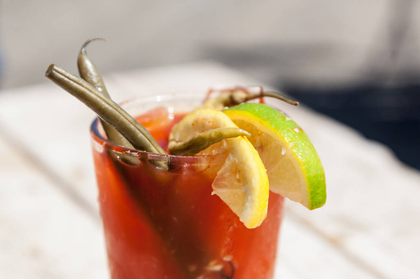 A fancy bloody mary cocktail sits on a wooden table outdoors. - Photo, Image