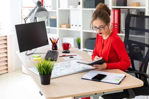 ein junges Mädchen sitzt an einem Tisch im Büro, hält einen Filzstift in der Hand und arbeitet mit Notizblock und Magnettafel. - Foto, Bild