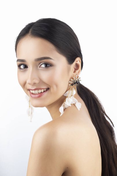 Beauty portrait of a beautiful smiling brunette girl model with bare shoulders and brown eyes wearing earrings imitation jewelry isolated on white background. Commercial design. Copy space. - Fotó, kép