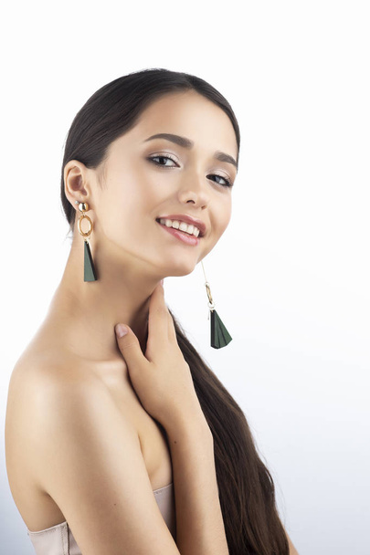 Beauty portrait of a beautiful smiling brunette girl model with bare shoulders and brown eyes wearing earrings imitation jewelry isolated on white background. Commercial design. Copy space. - Photo, image