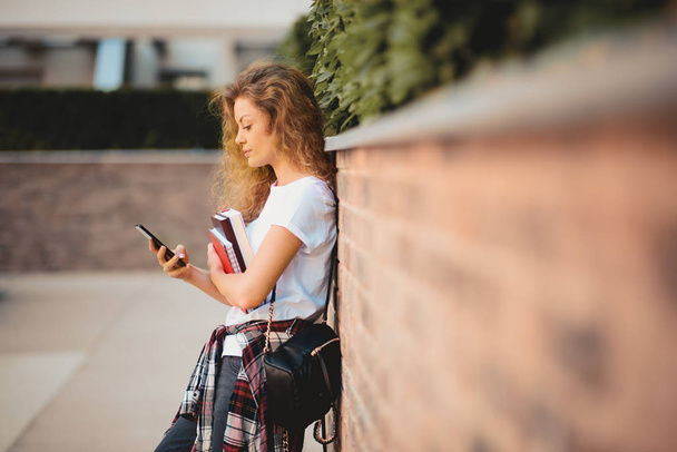 Studentessa che usa lo smart phone e tiene libri mentre cammina nel campus
. - Foto, immagini