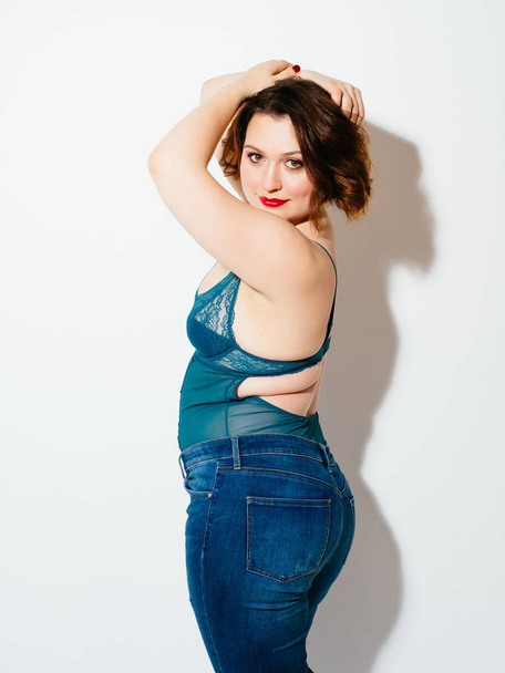 Side view of beautiful plus size woman wearing delicate underwear and jeans and looking at camera while standing on white background - Foto, immagini