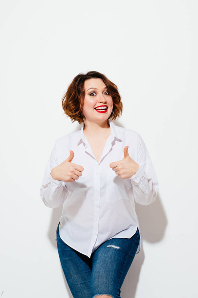 Beautiful plump female cheerfully smiling and showing thumb-up gesture while standing on white background and looking at camera - Zdjęcie, obraz