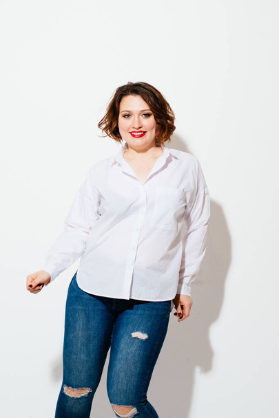 Cute plus size woman in casual outfit smiling and looking at camera while actively dancing on white background - Photo, Image