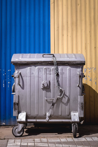 Sarı ve mavi arka plan üzerinde büyük metal tekerlekli atık konteyner - Fotoğraf, Görsel