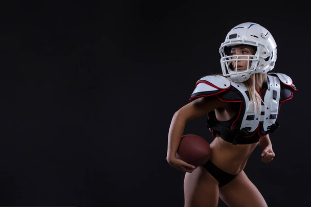 Спортивная серьезная женщина в шлеме регбиста, держащая мяч в студии на тёмном фоне. Спортсменка. Гендерное равенство. Копирование пространства
 - Фото, изображение