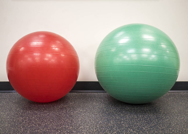 Malá červená kulová koule vedle středně velké švýcarské koule v tělocvičně - Fotografie, Obrázek