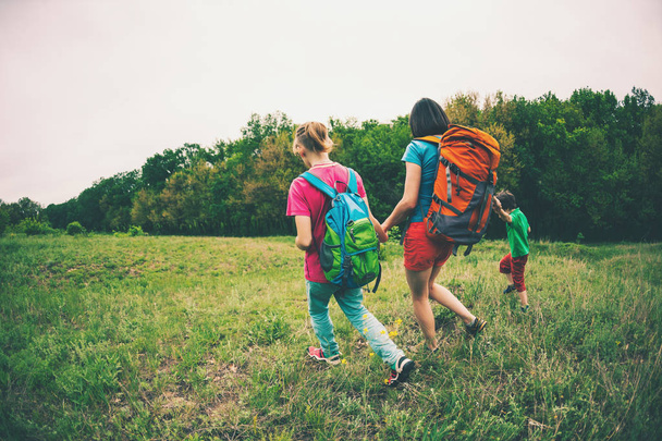 A woman with children goes hiking. The woman took her sons by the arms. Traveling with family. The boy walks with his brother and mother in the forest. Hike with backpacks. - Photo, Image