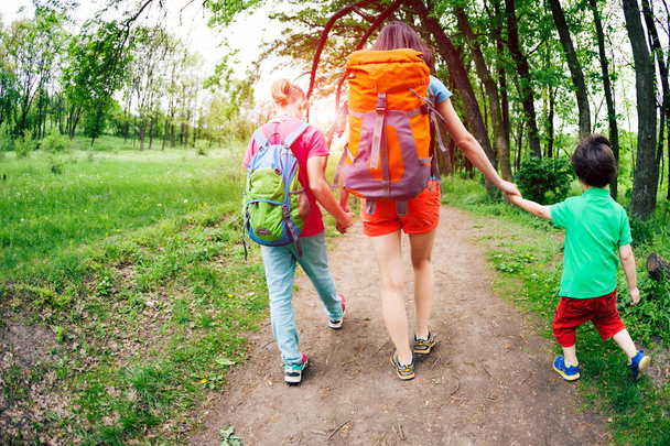 A woman with children goes hiking. The woman took her sons by the arms. The family goes on a dirt road. The boy walks with his brother and mother in the forest. Hike with backpacks. - Photo, Image