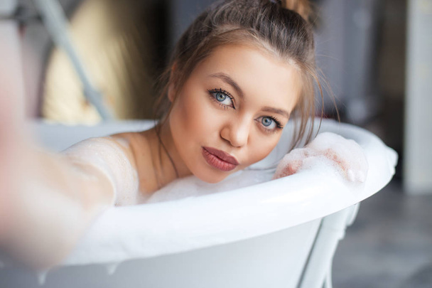 beautiful brown-haired girl with full lips taking self pictures in the bath. close-up photo. selfie conceept. take a picture in the bathroom - Фото, зображення