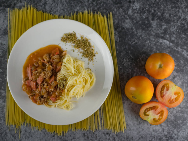 érett főtt tészta spagetti Paradicsom szósz oregano fehér lemez. nyers spagettit és paradicsom mellett. - Fotó, kép