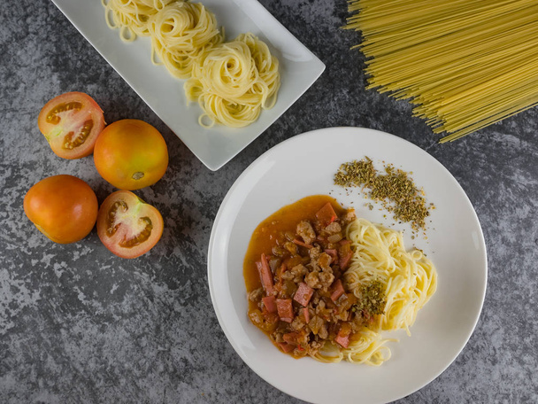 érett főtt tészta spagetti Paradicsom szósz oregano fehér lemez. nyers spagettit és paradicsom mellett. - Fotó, kép