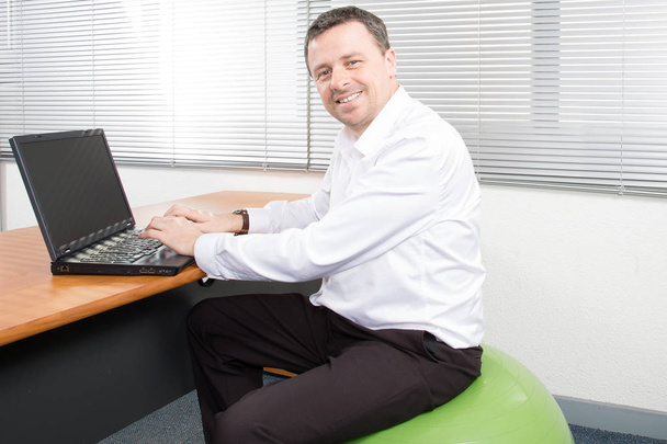 zakenman op stabiliteit bal werkende laptop in zijn kantoor - Foto, afbeelding