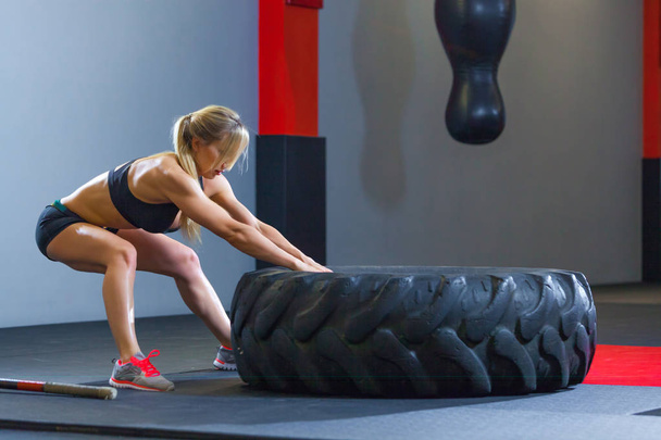 Fit female athlete working out with a huge tire, pulls in the gym. Crossfit woman exercising with big tire - Foto, immagini