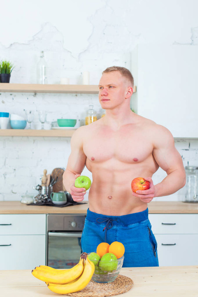 Muscular man with a naked torso in the kitchen with fruit, concept of healthy eating. Athletic way of life. - Foto, imagen