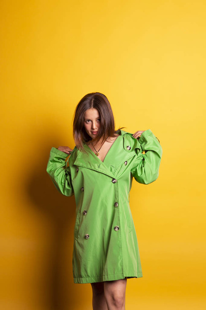joven bonita mujer usando piel de aceite verde con capucha posando sobre fondo amarillo
  - Foto, Imagen
