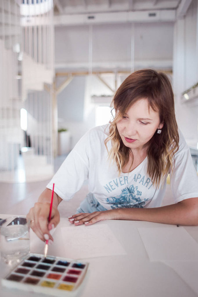 молода жінка малює фотографію водяного кольору. Вид спереду на малювання дівчини з водяним кольором на столі. Художник малює картину в студії
 - Фото, зображення