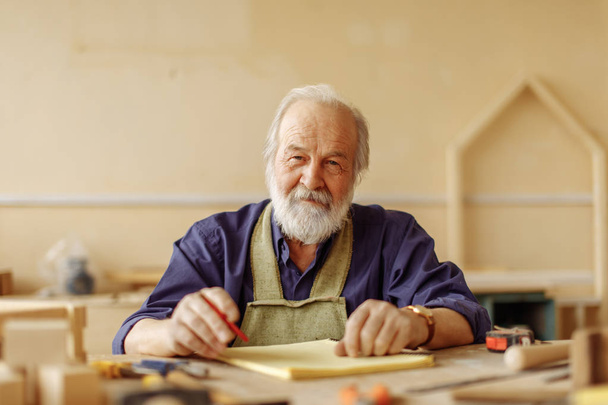 old journeyman with many wrinkles sitting at the desk with tools - Foto, Imagen
