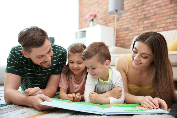Νεαρό ζευγάρι ανάγνωση το βιβλίο με τα παιδιά στο σπίτι. Ευτυχισμένη οικογένεια - Φωτογραφία, εικόνα
