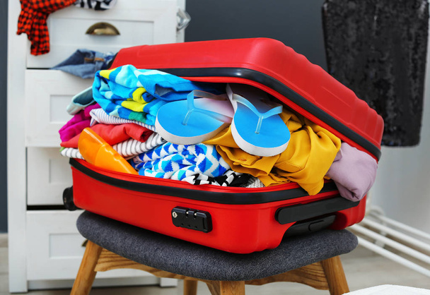 Suitcase with beach clothes and accessories on stool indoors - Foto, Bild