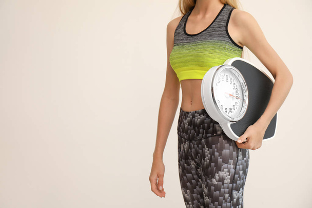 Woman holding scales on light background. Healthy diet - Foto, afbeelding