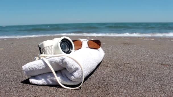 φωτογραφική μηχανή με γυαλιά πάνω στην αμμώδη παραλία και παραλία ψέματα - Πλάνα, βίντεο