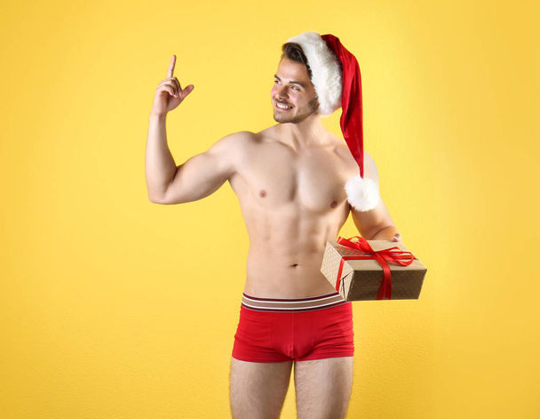 Shirtless sexy young Santa Claus with gift on color background - Φωτογραφία, εικόνα