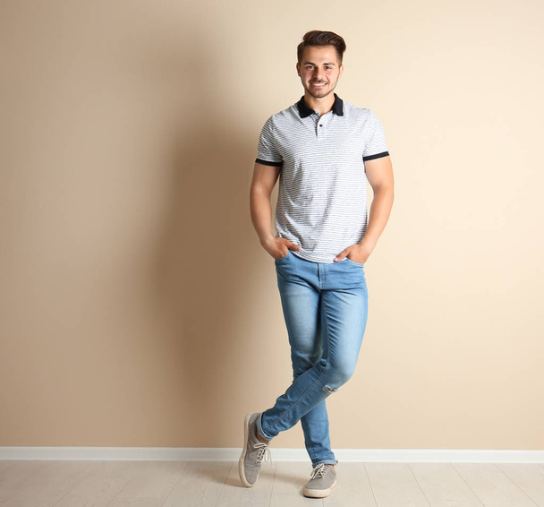 Young man in stylish jeans near light wall - Foto, Bild