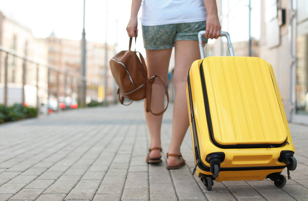 Young woman with yellow carry on suitcase outdoors - Foto, imagen