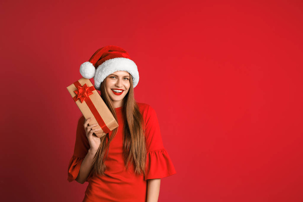 Young beautiful woman in Santa hat with gift box on color background. Christmas celebration - Photo, Image