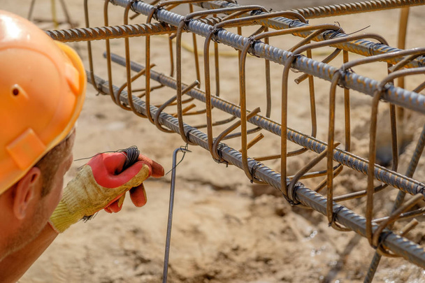 Rukou pracovníka v ochranné rukavice úplet kovové tyče s drátem pro vyztužení betonu. Detailní pohled - Fotografie, Obrázek