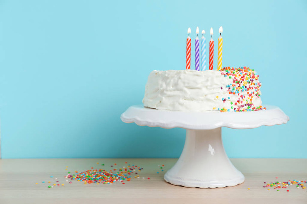 Birthday cake with candles on table against color background - Fotoğraf, Görsel