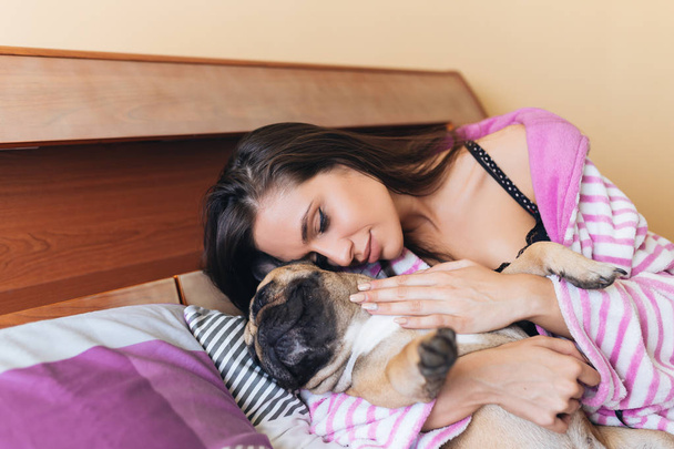 Atrakcyjna, młoda kobieta, ciesząc się na łóżku z jej zwierzętom Buldog francuski.  - Zdjęcie, obraz