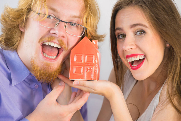 A boldog fiatal pár készen áll az együttélésre. Egy férfi és egy nő kis piros házi modellel. Lakástulajdon, ingatlan koncepció. - Fotó, kép