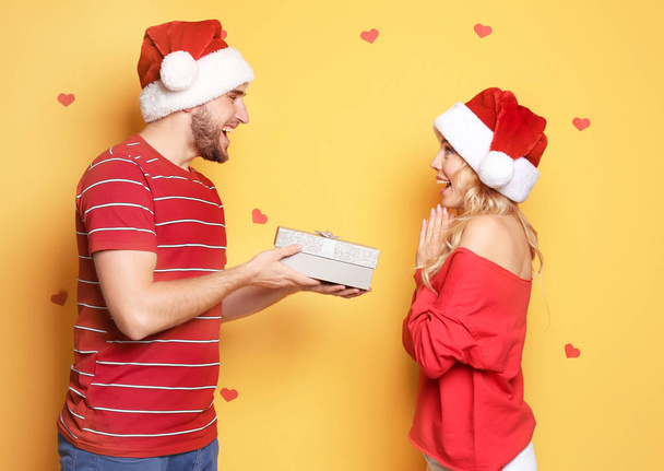 Young couple in Santa hats with Christmas gift on color background - Foto, immagini