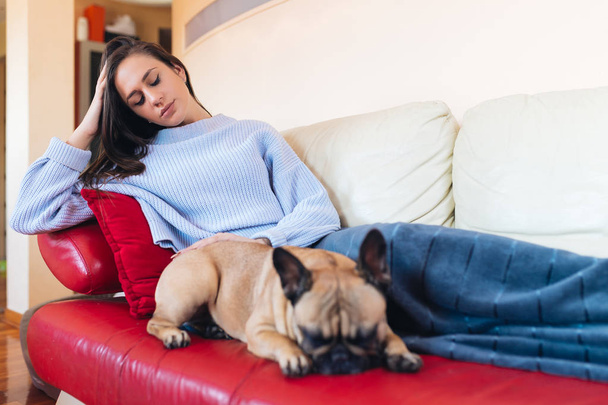 Attraente giovane donna sdraiata sul divano con il suo animale domestico bulldog francese e riposo
.  - Foto, immagini