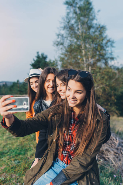 Чотири молоді дівчата насолоджуються на відкритому повітрі і приймають селфі з мобільним телефоном
 - Фото, зображення