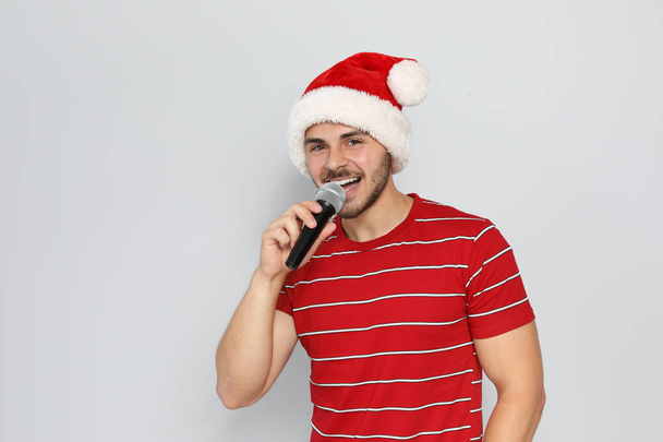 Young man in Santa hat singing into microphone on color background. Christmas music - 写真・画像